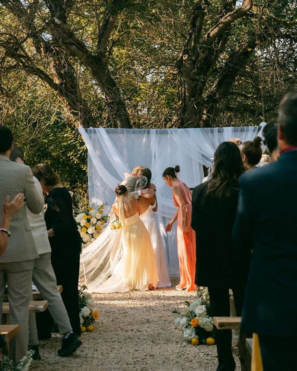 Cérémonie de mariage émouvante sous les arbres avec voilages et fleurs blanches à la Bastide de Lussan