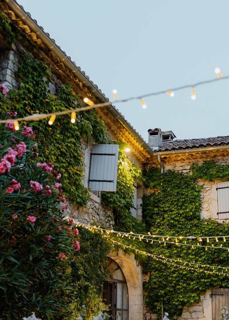 Mas provençal avec des vignes qui grimpent sur la façade, du lierre rose, des volets en bois et des guirlandes lumineuses